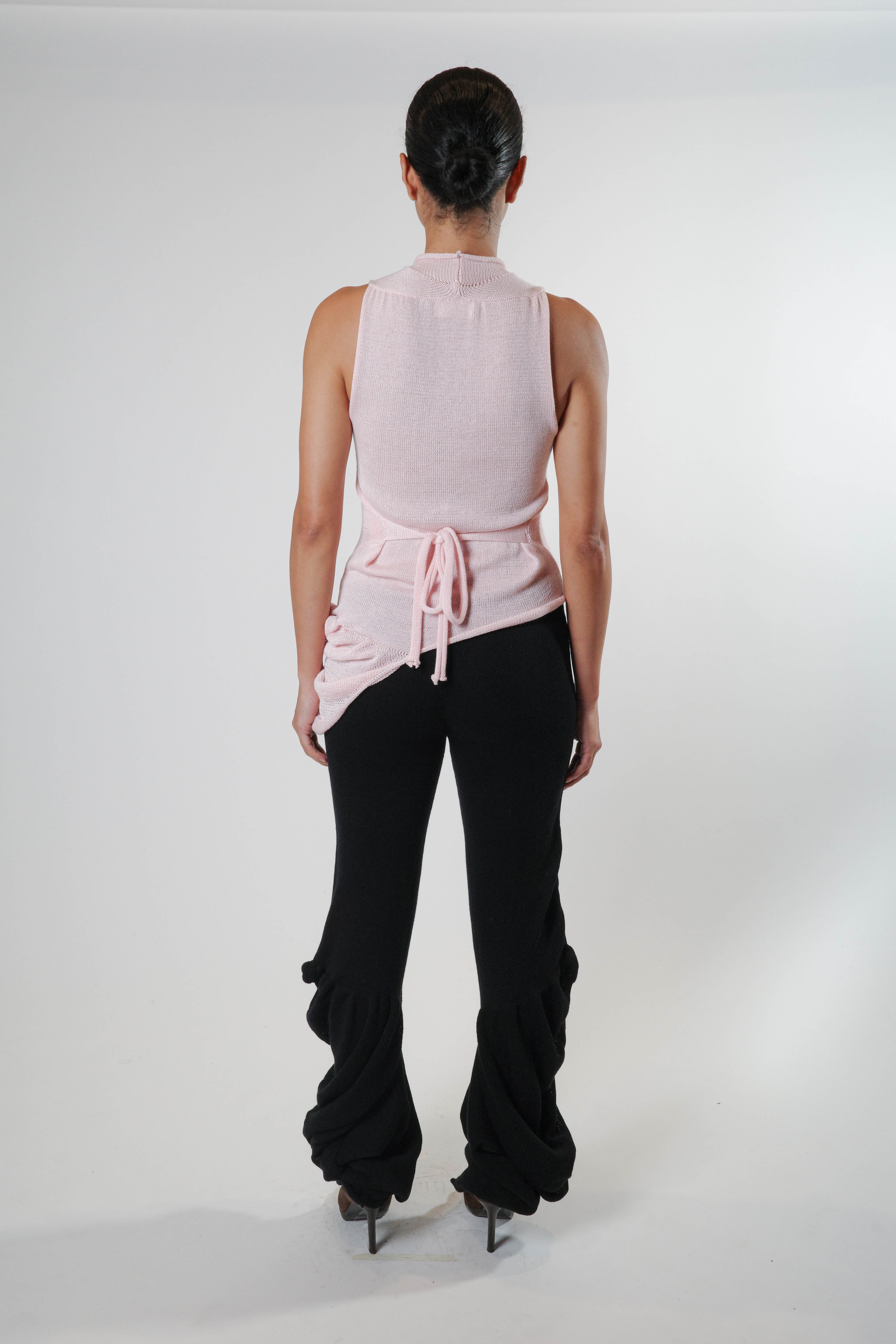 Back view of black knit pants with draped side detailing and elongated silhouette, styled with pink knit tank top