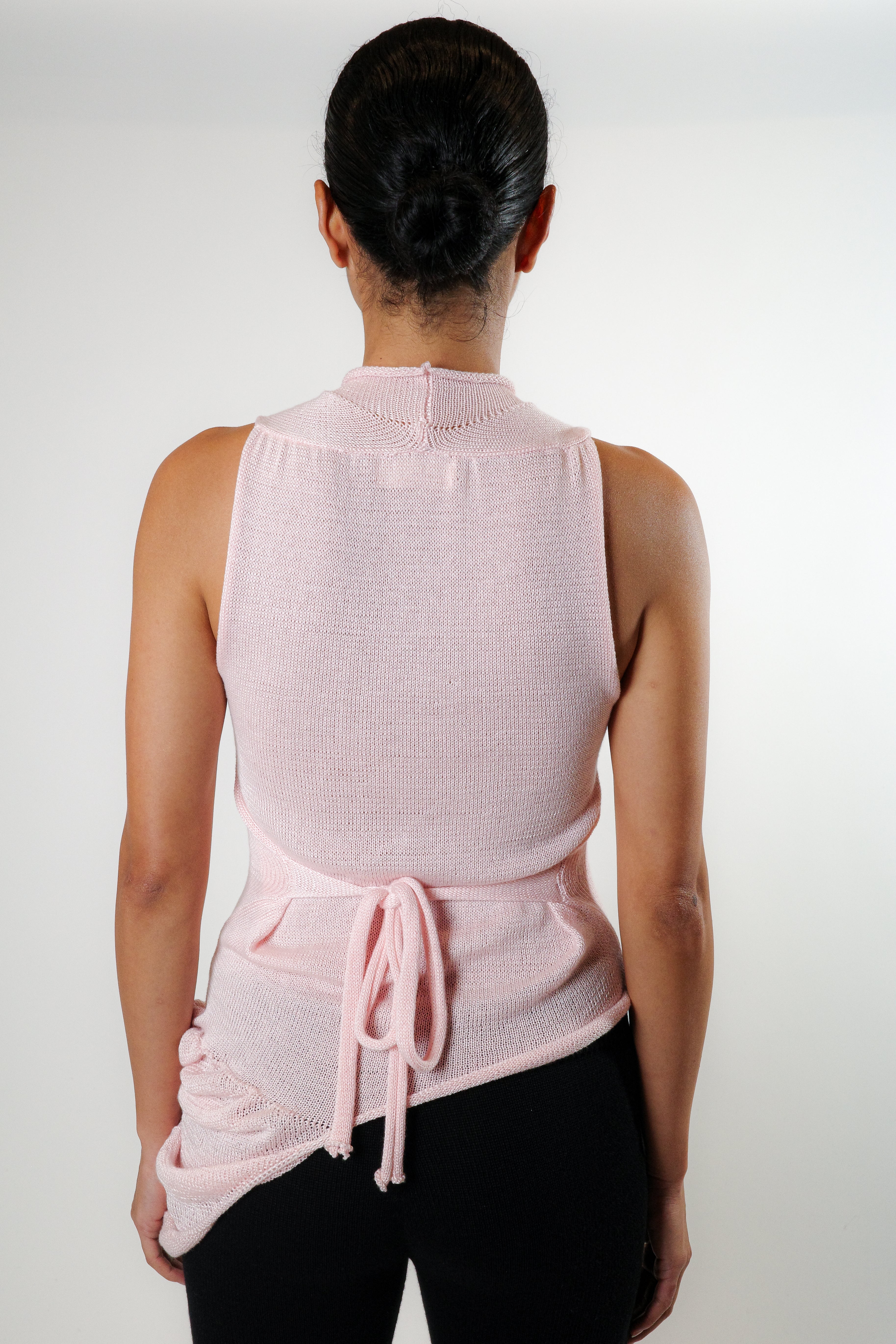 Back view of pink knit top with side ties and fitted silhouette, paired with black knit pants