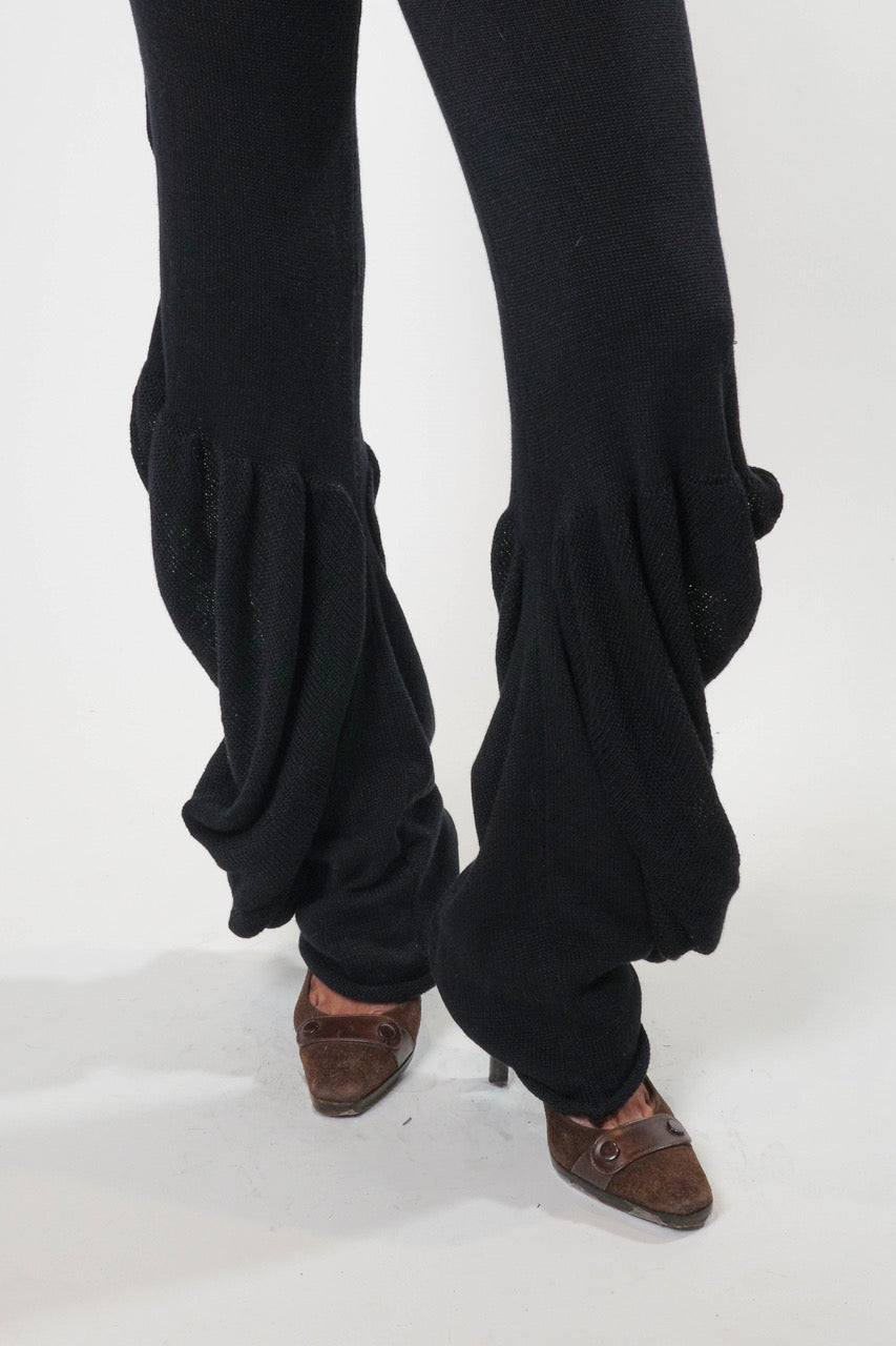 Black knit pants with draped side detailing and gathered silhouette, worn full length