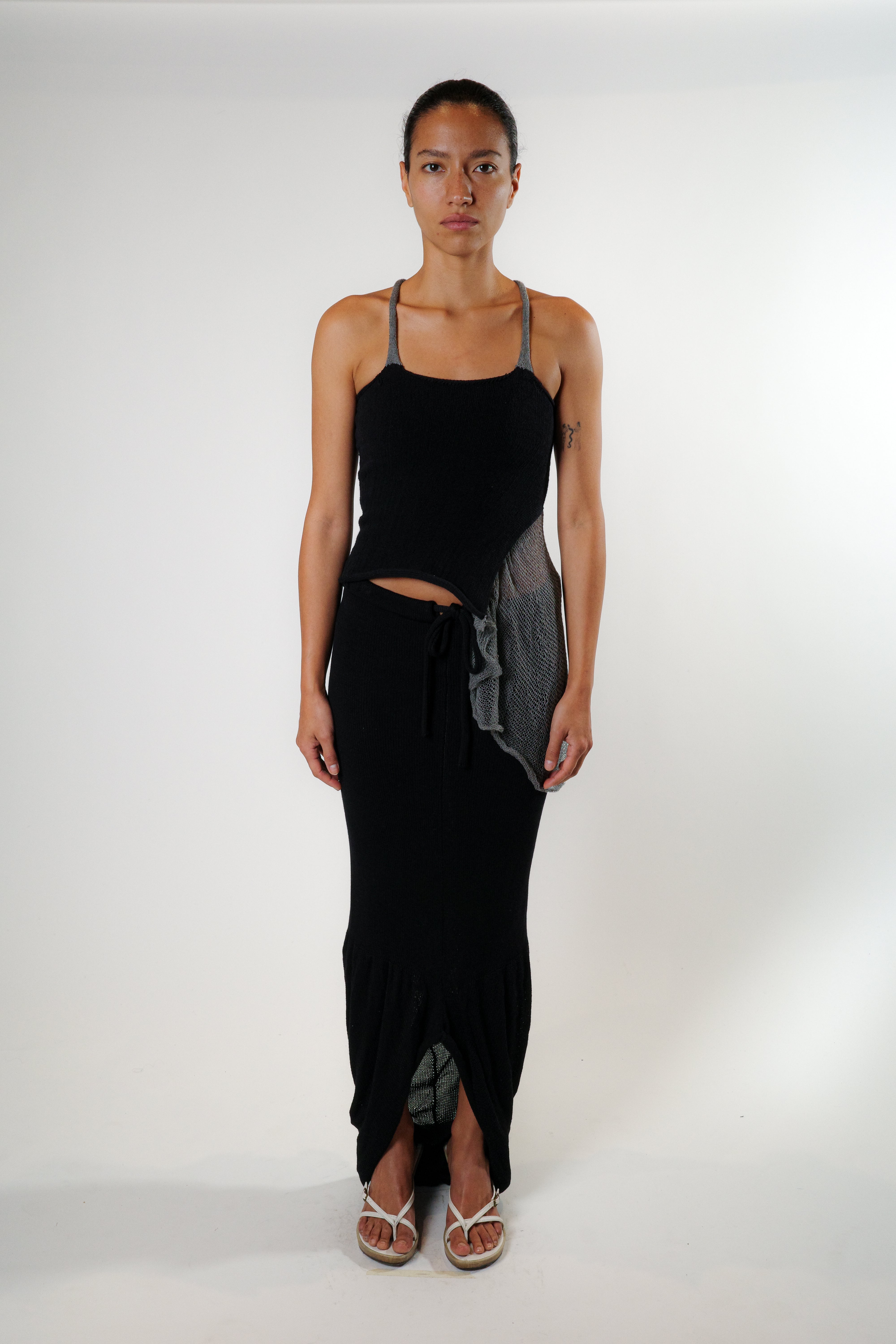 Full body view of black knit top with draped side detail and contrast panel, styled as a dress