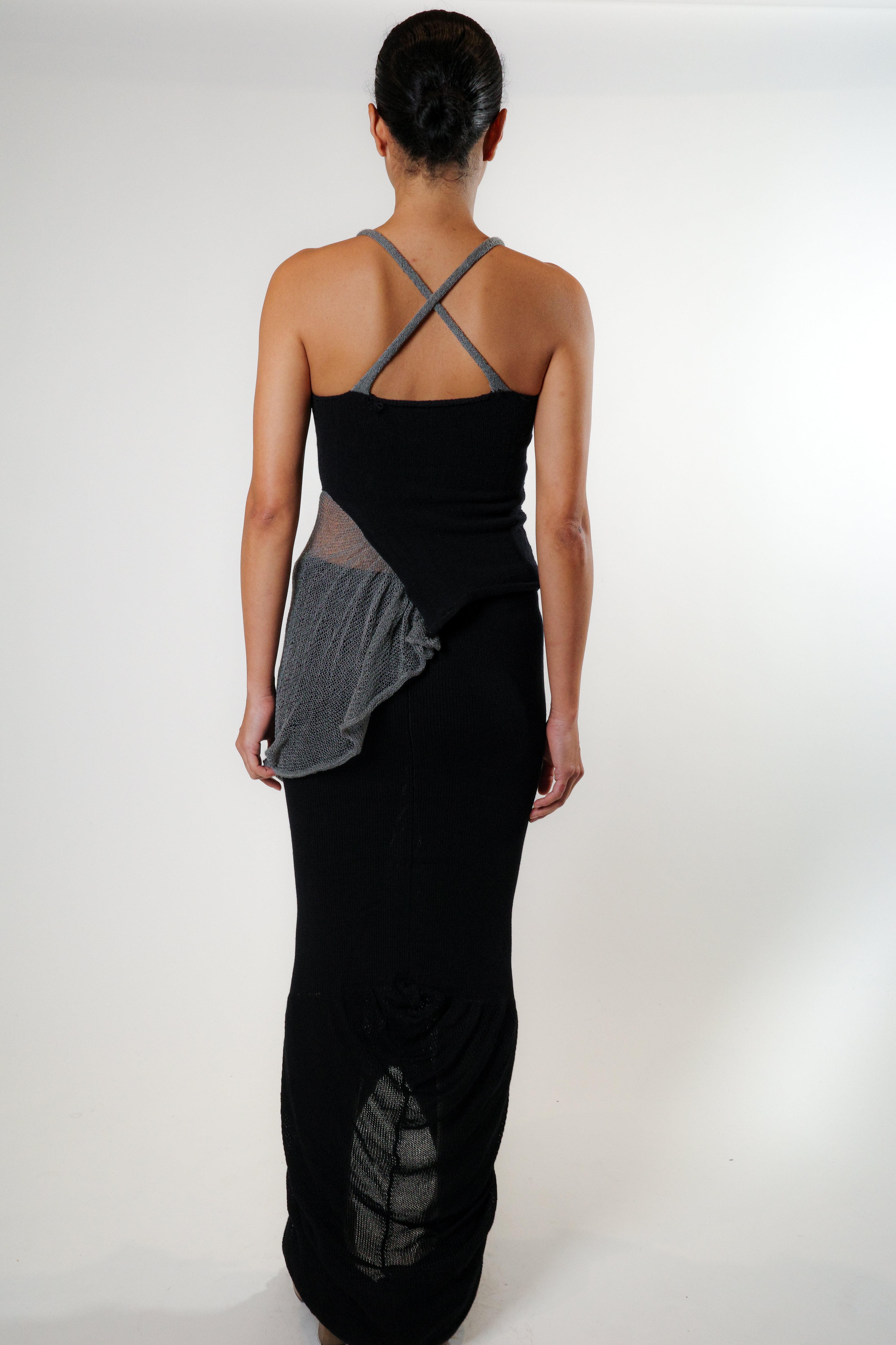 Back view of black knit top with X shaped back and draped side detail, elongated silhouette