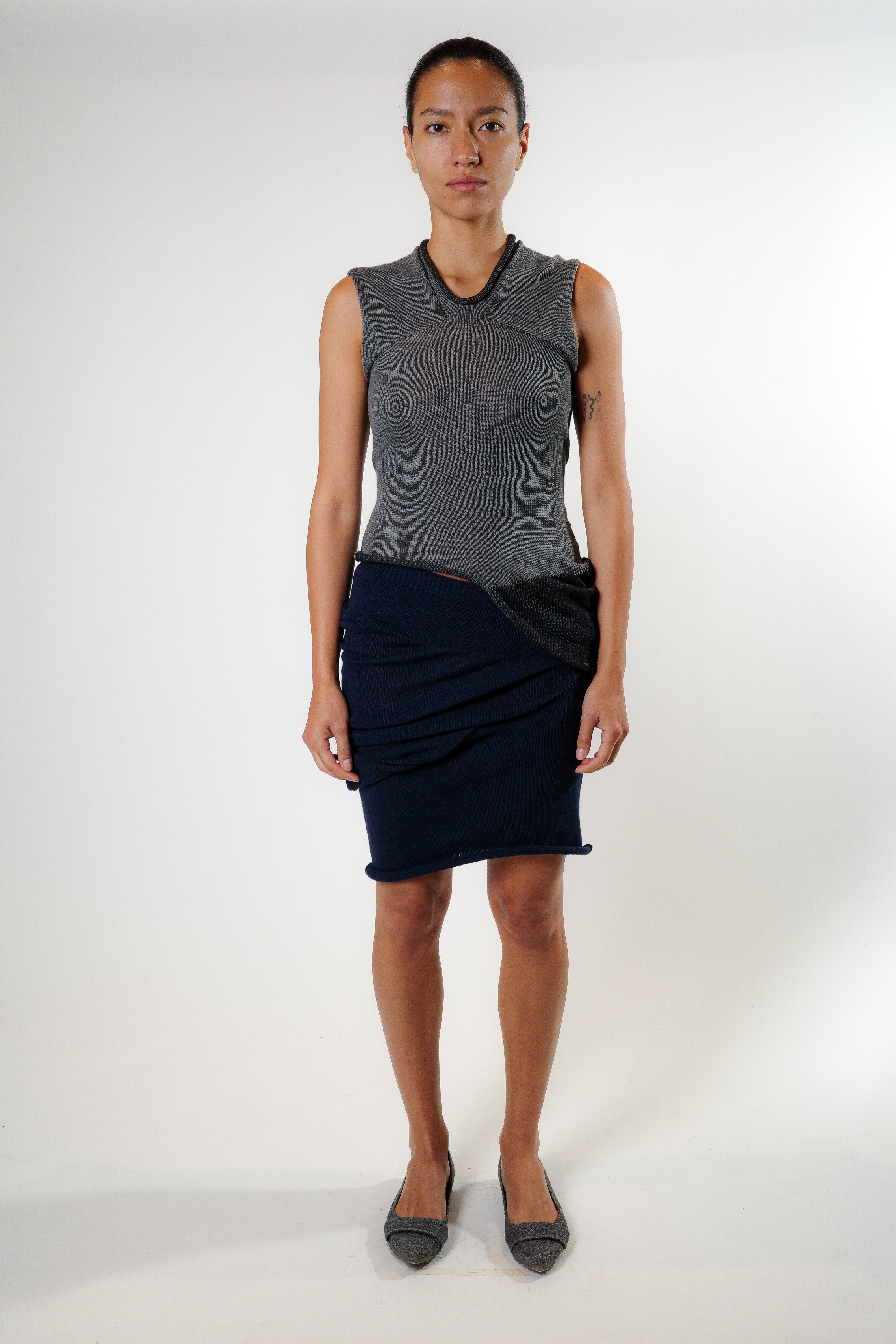 Full body view of grey reversible knit top styled with navy skirt, fluid silhouette