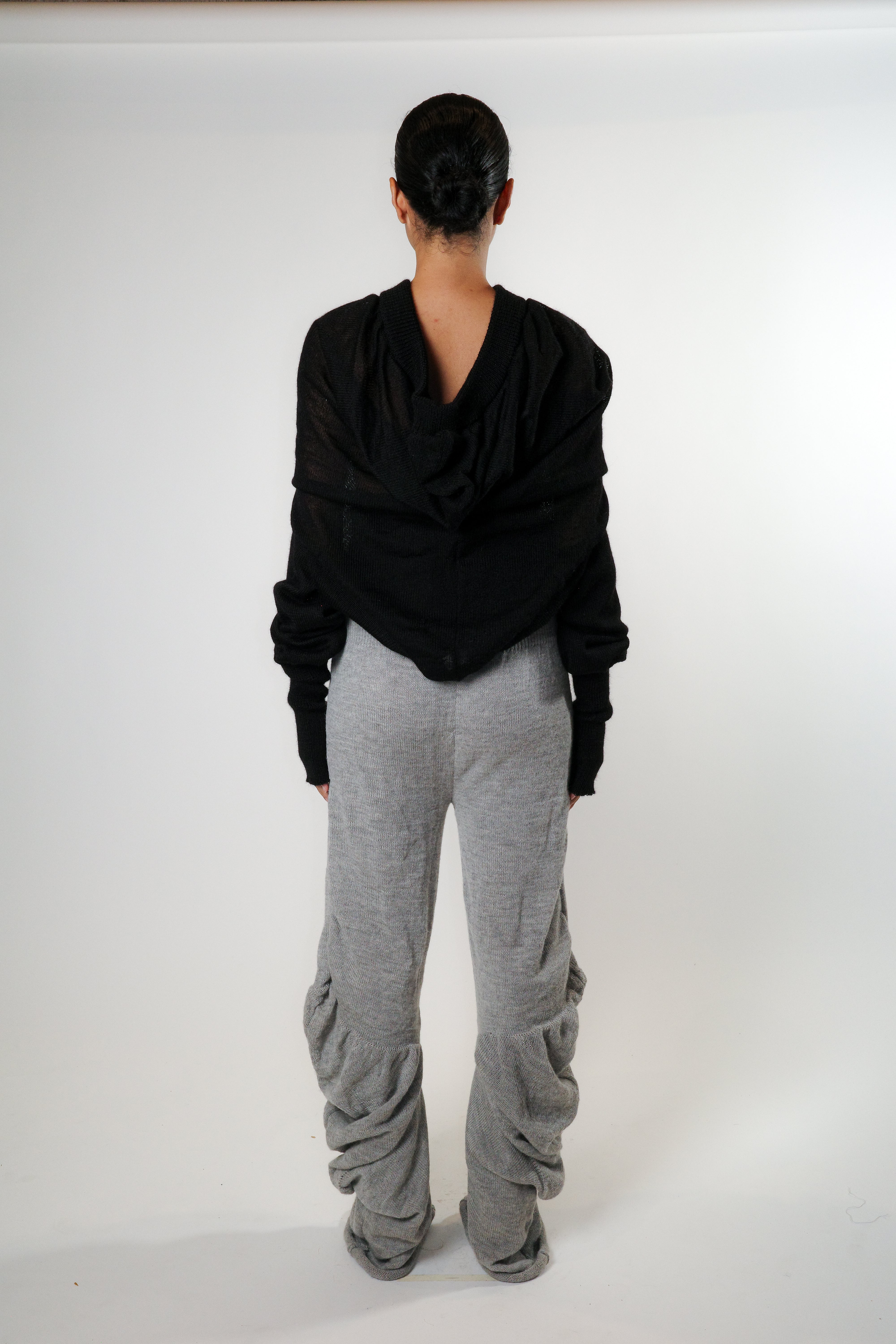 Back view of black knit triangle hoodie with soft draped back and ribbed hem, styled with grey knit pants